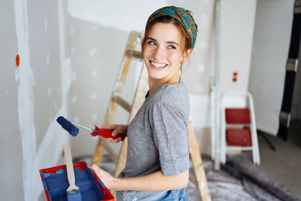 smiling young woman with paint roller doing renovations